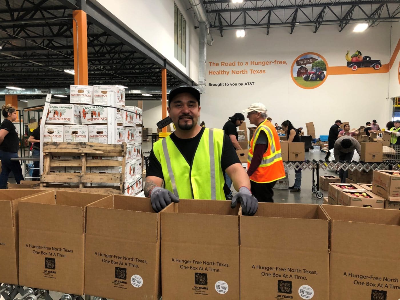 Man in a yellow vest packing boxes of food at the North Texas Food Bank