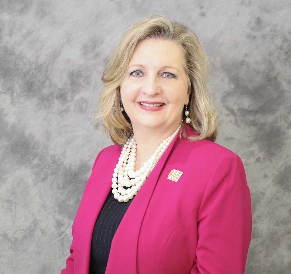 Trisha Cunningham in a pink blazer and pearl necklack against a grey background