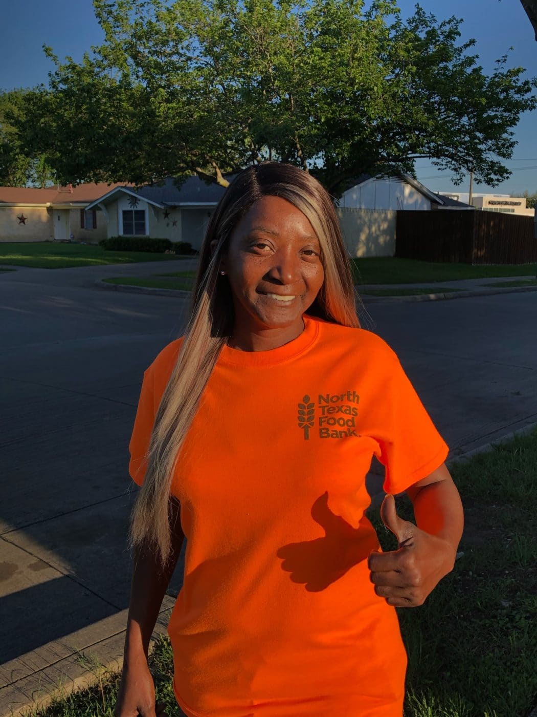 Woman wearing an orange North Texas Food Bank t-shirt smiling and giving a thumbs up