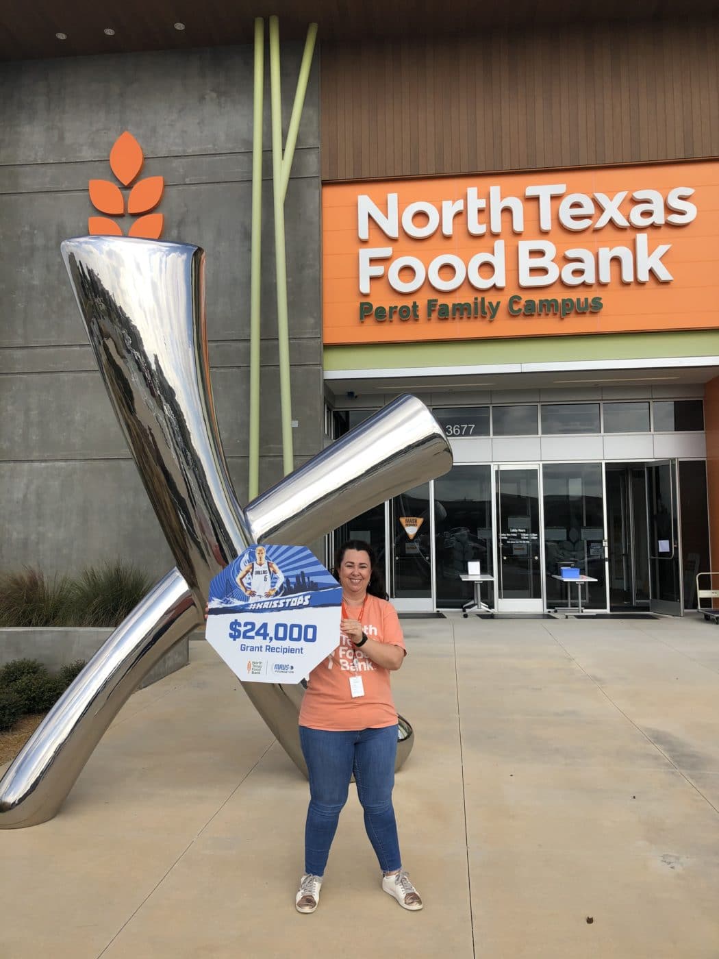 Zahra standing outside of the North Texas Food Bank's Perot Famiy Campus holding a $24,000 Grant from the Dallas Mavericks