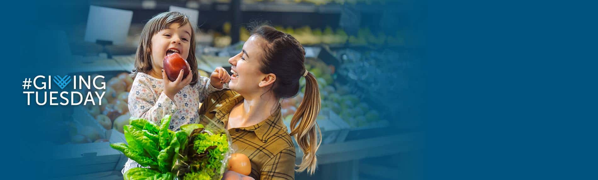 Woman holding young girl in grocery store eating an apple