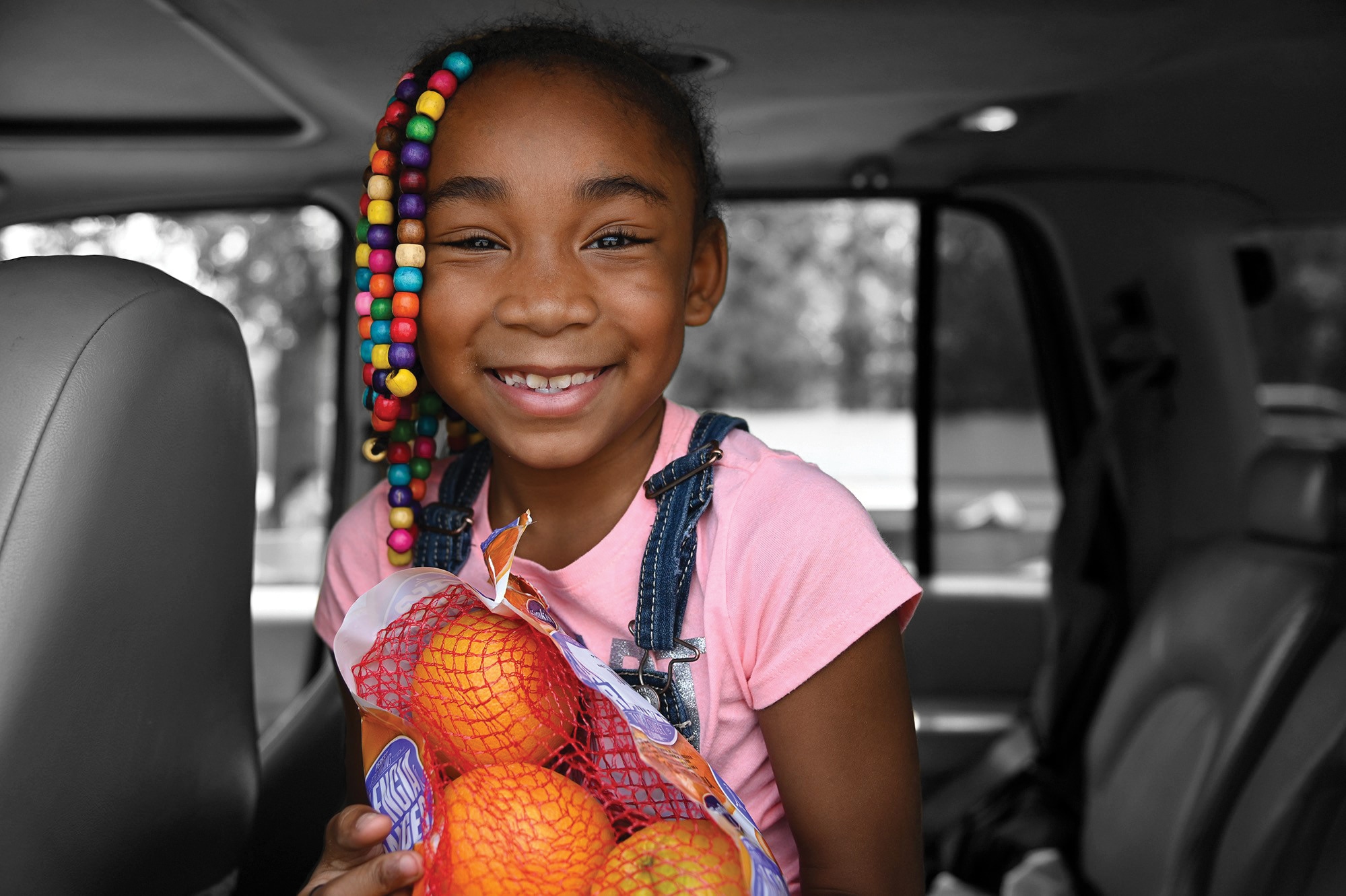 Young girl sitting in a car holding a bag of oranges