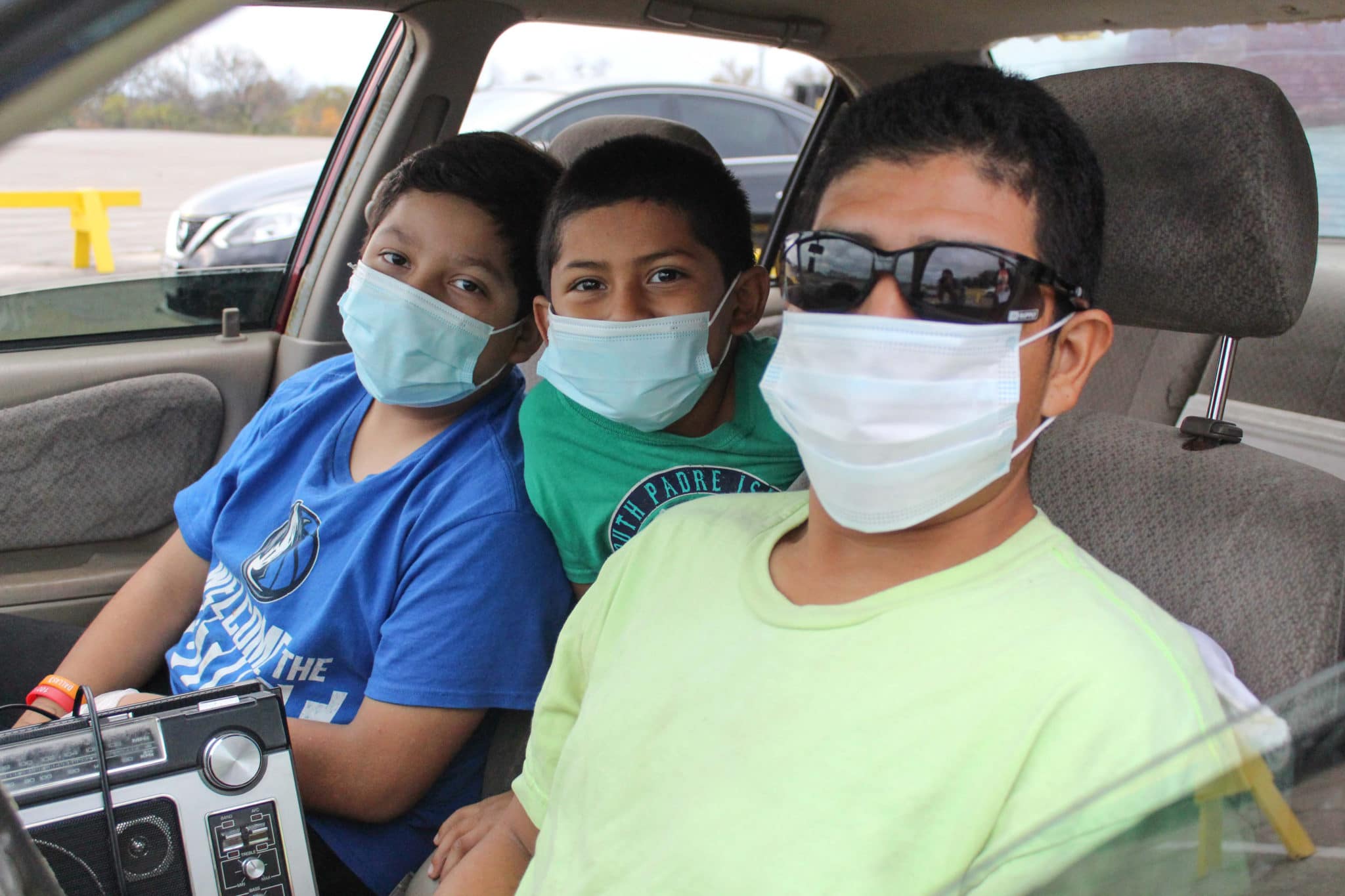 Father and two sons sitting in their car with masks on