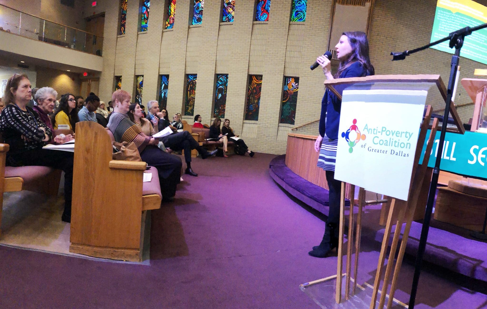 Valerie Hawthorne speaking on a microphone at the Anti-Poverty Coalition of Greater Dallas Lecture Series