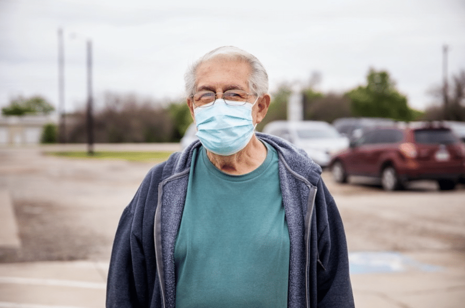 Old white man with white hair wearing a mask outside