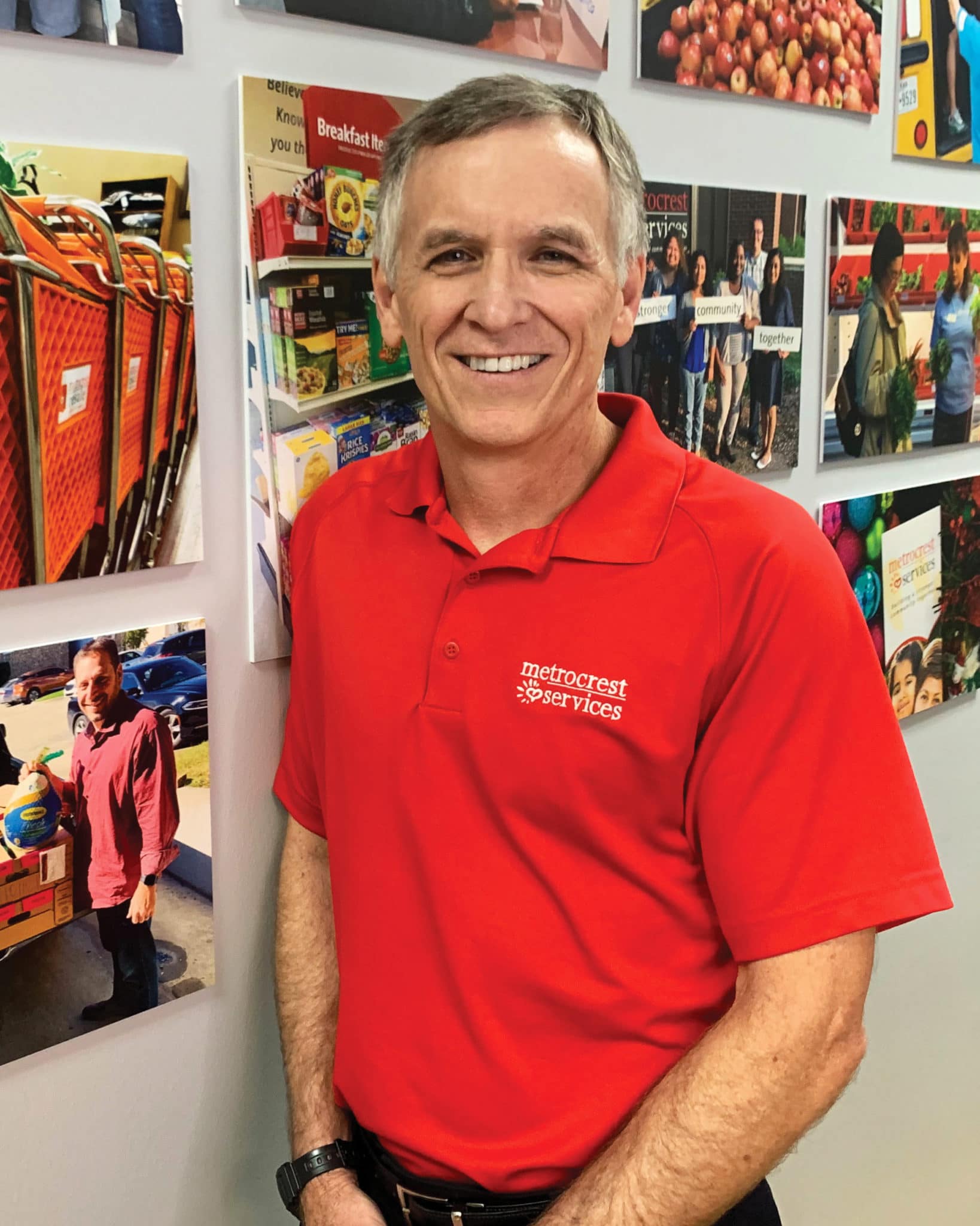 White man in a red polo shirt leaning against a wall with hanging pictures