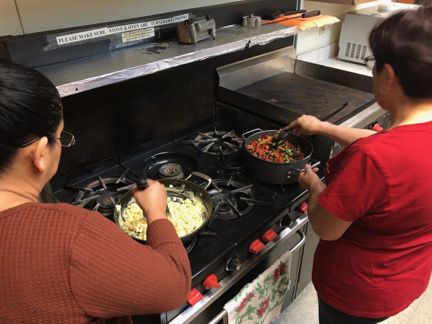 Two women cooking dishes at stove.
