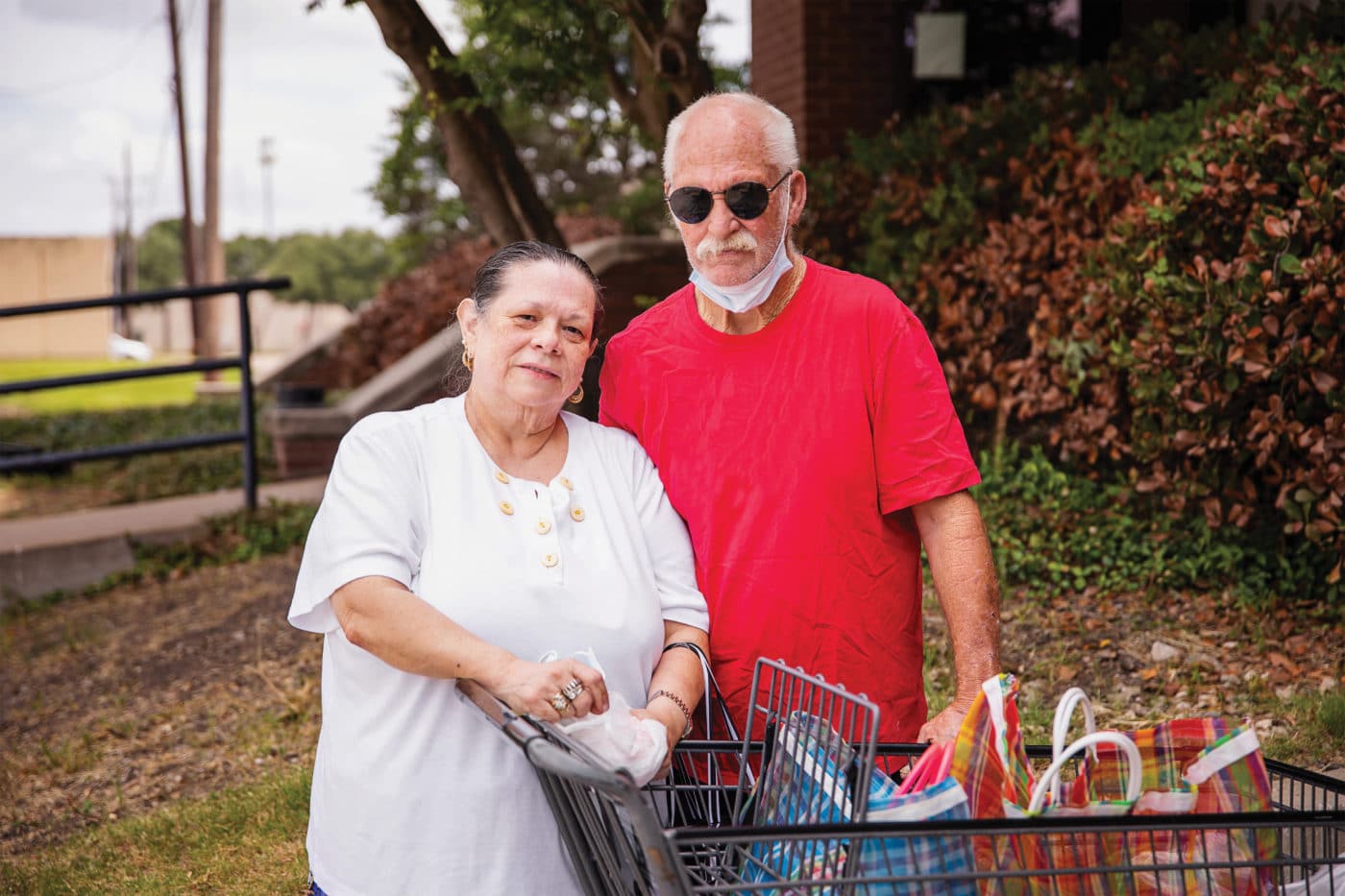Woman in white shirt next to man in red t-shirt by grocery cart.