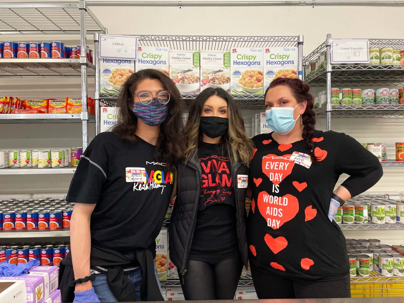 Three women with masks on standing in food pantry in front of shelves of canned and box goods.