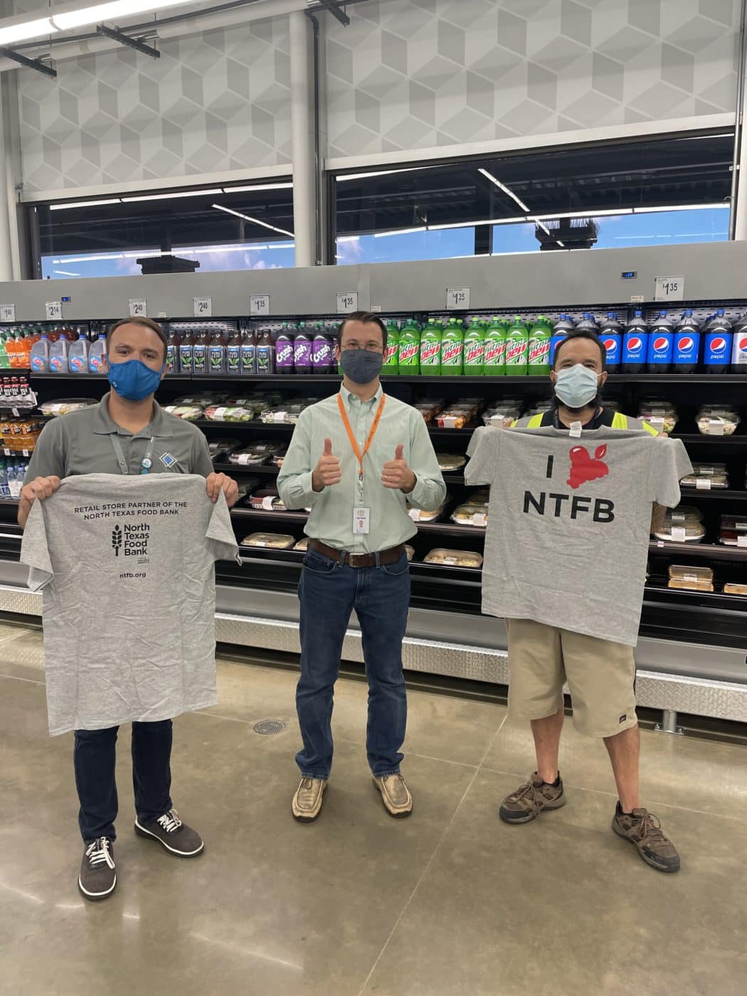 Three men standing and holding t-shirts in a grocery store.