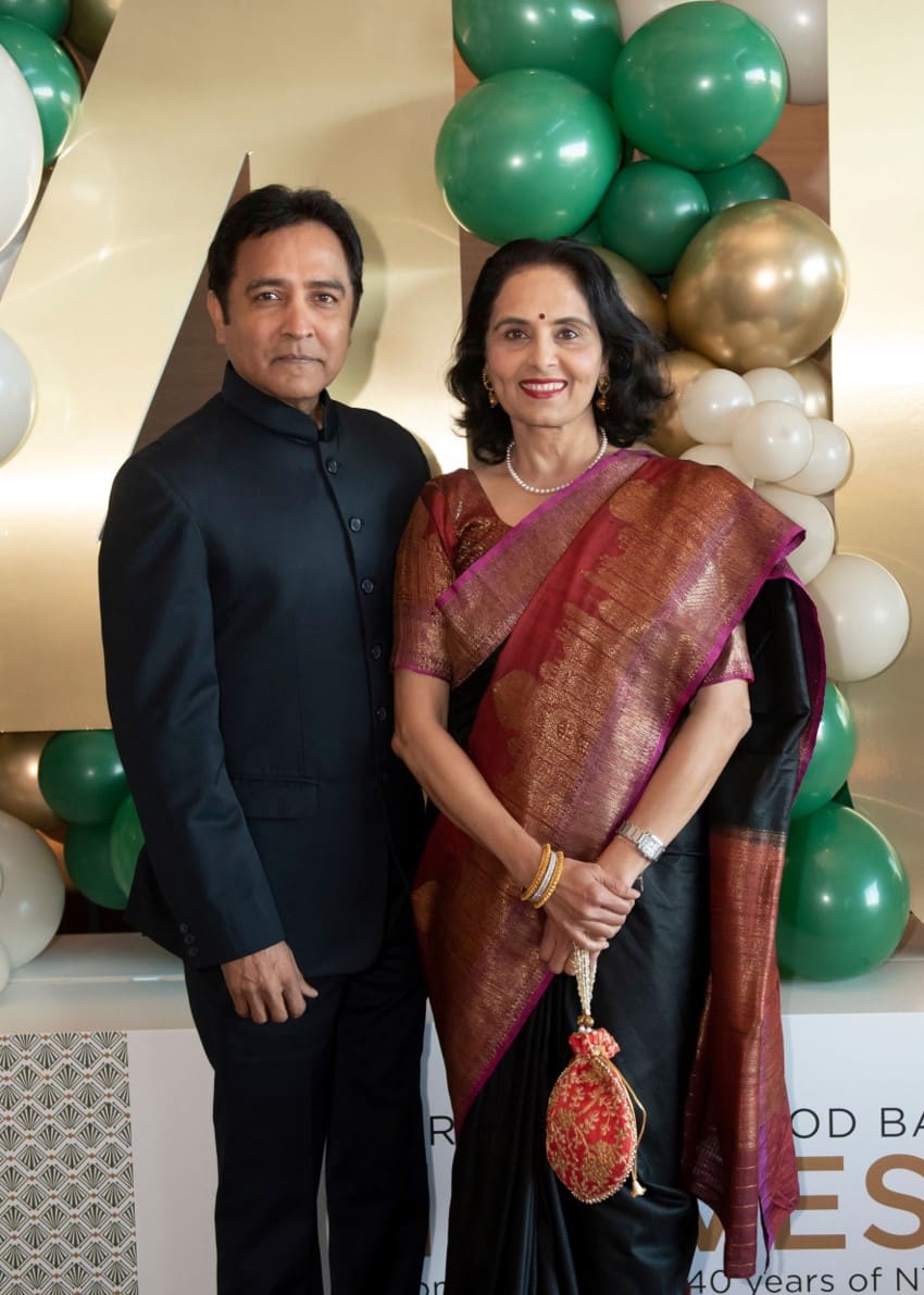 Man in black suit and woman in dress in front of gold and green balloons