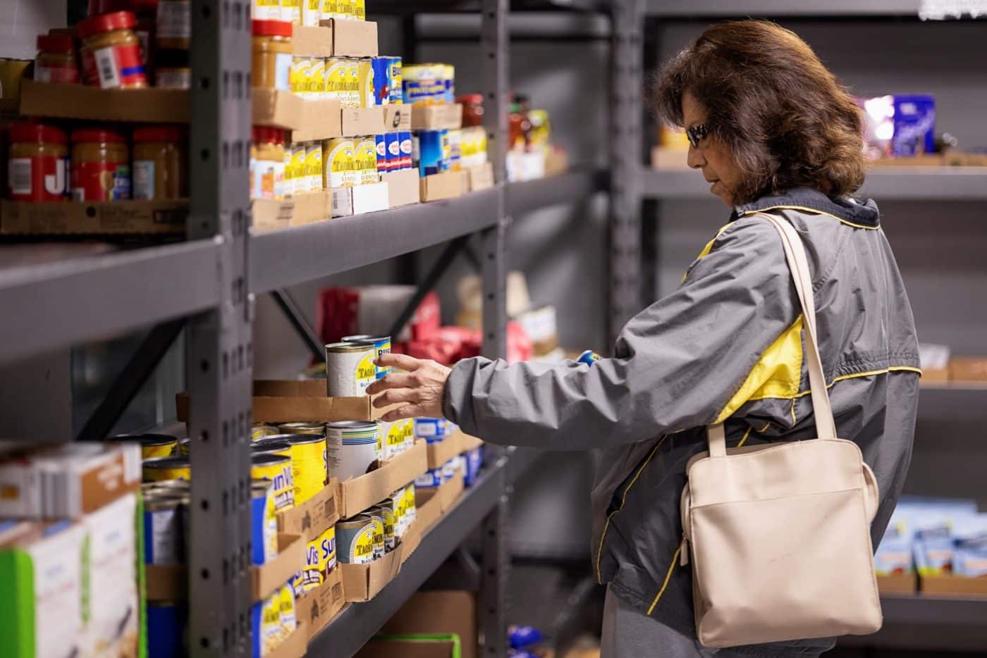 Woman with grey jacket and purse shopping for canned food