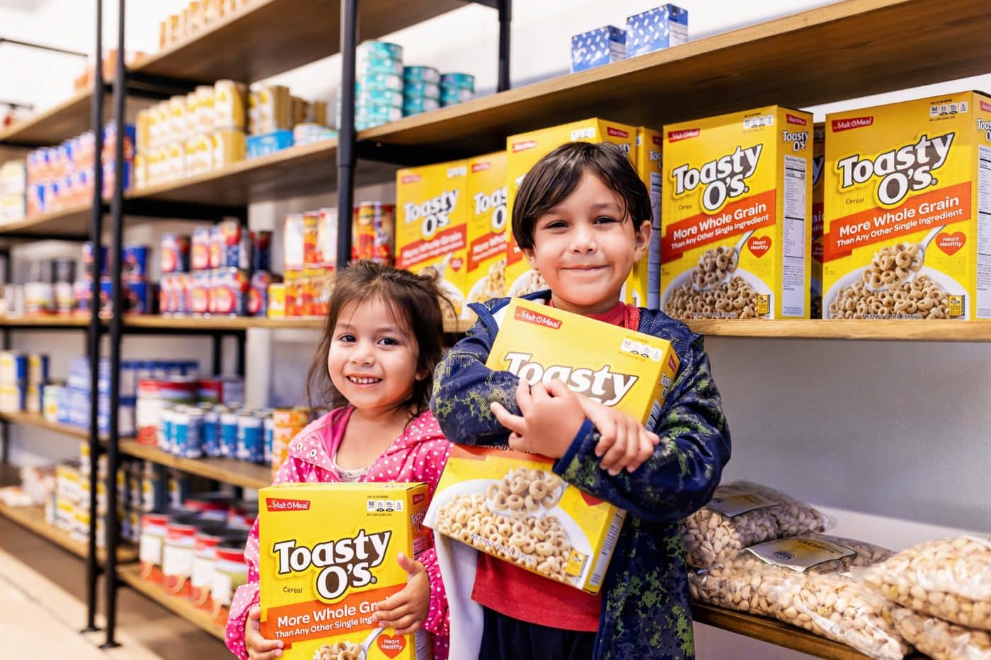 A young boy and girl holding cereal boxes in front of shelves of food.