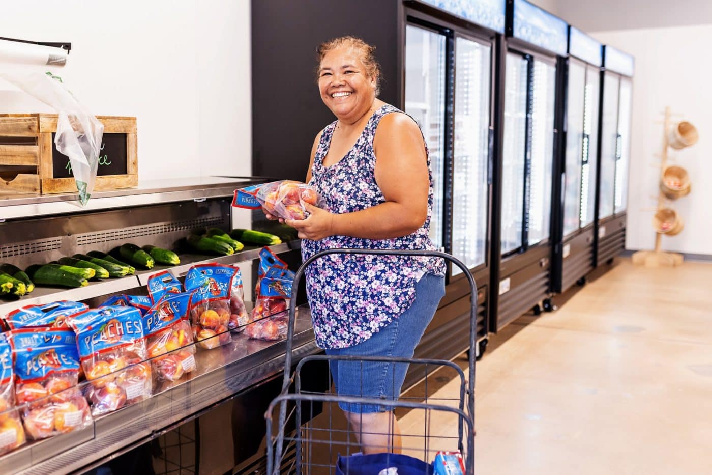 Woman smiling at grocery store holding bag of peaches.