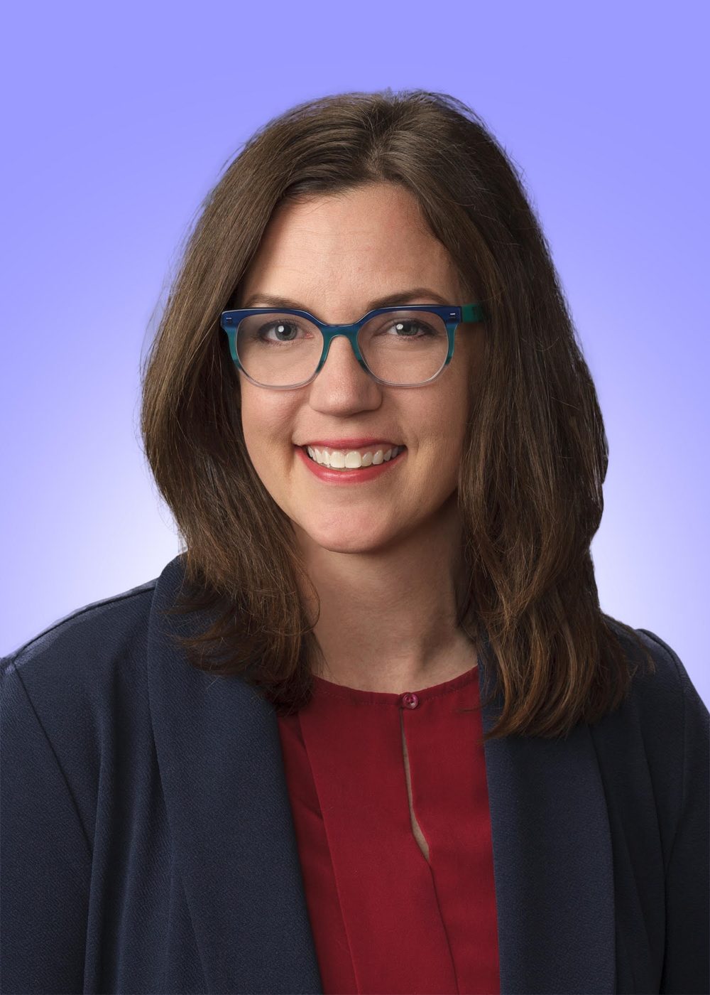 Headshot of woman with brown hair and glasses and red shirt and blue blazer