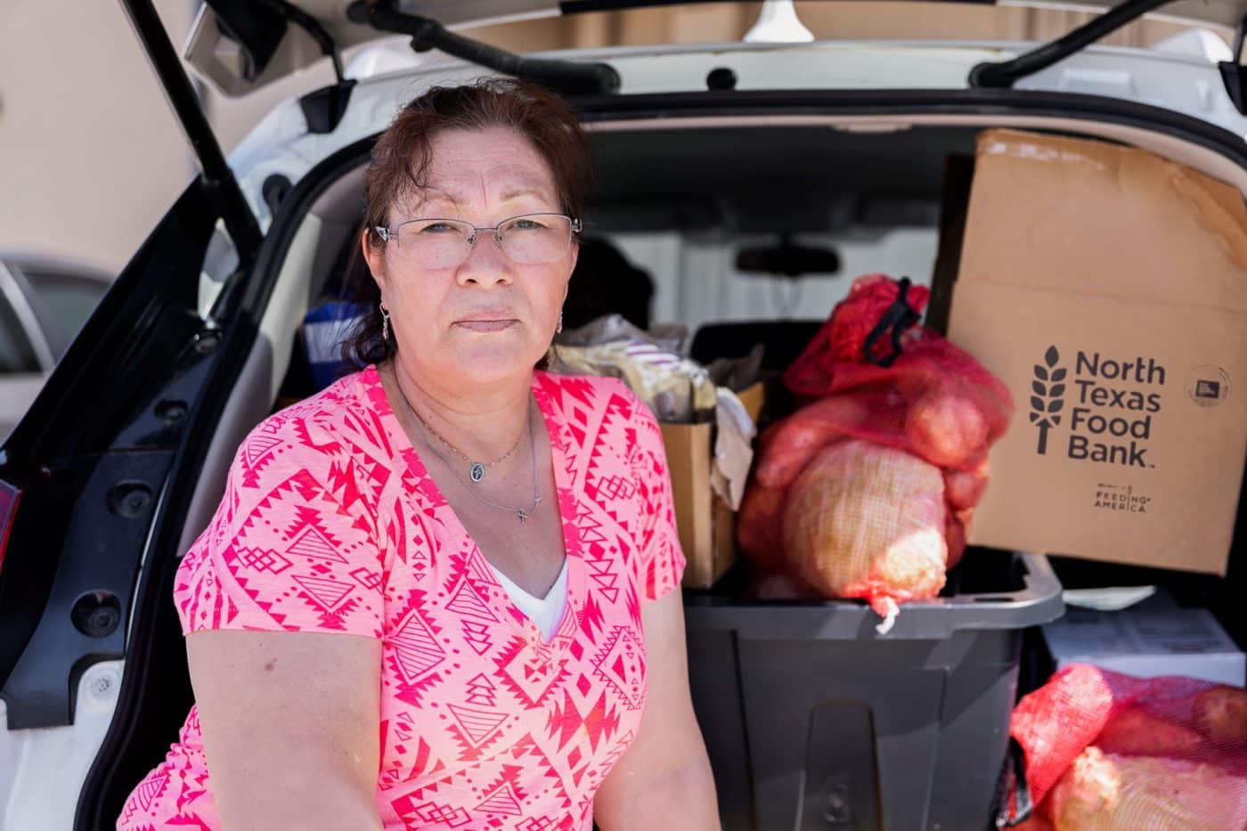 Women with pink and red shirt near car with food in the trunk