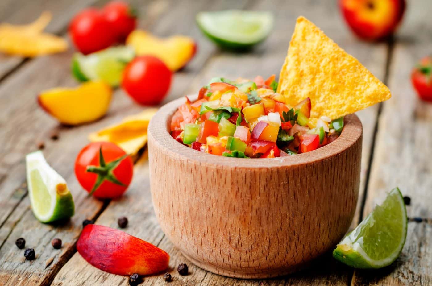 Peach salsa in wooden bowl with one chip sticking out of it