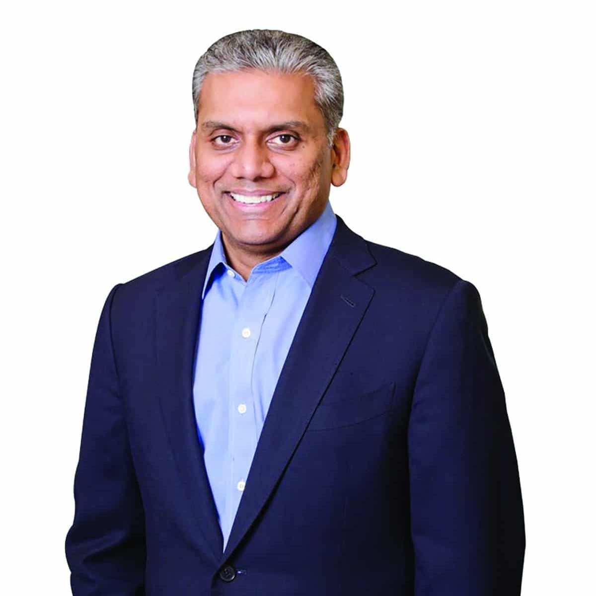 Anurag Jain smiling in a dark suit and blue button down shirt in front of a white background