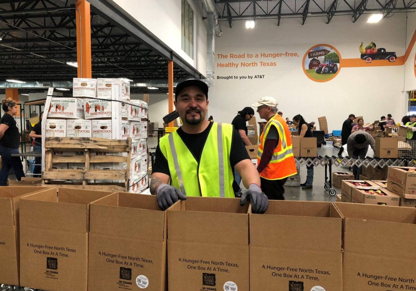 Man in a yellow vest packing boxes of food at the North Texas Food Bank