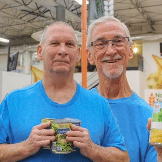 Two older white men in blue shirts holding canned goods