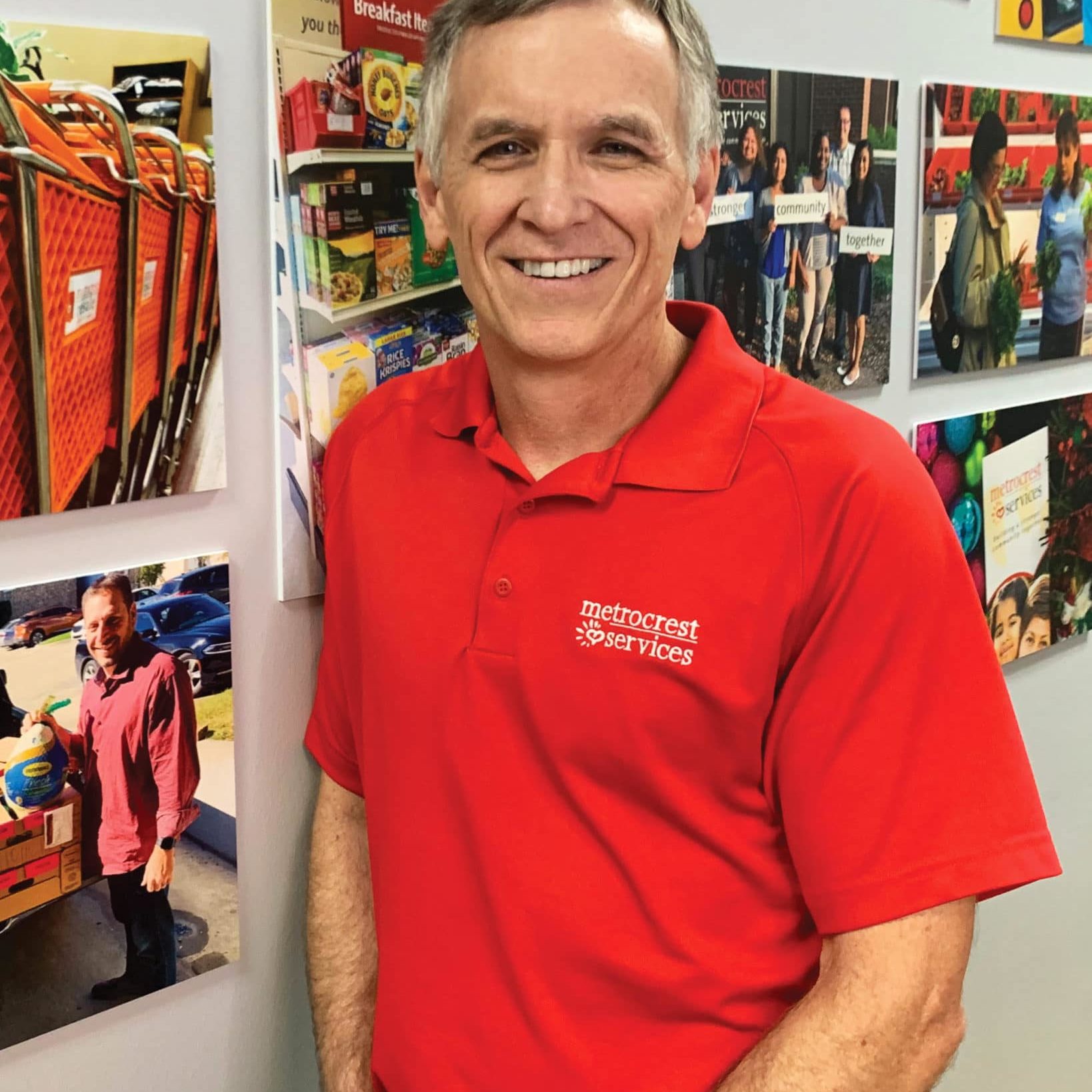 White man in a red polo shirt leaning against a wall with hanging pictures